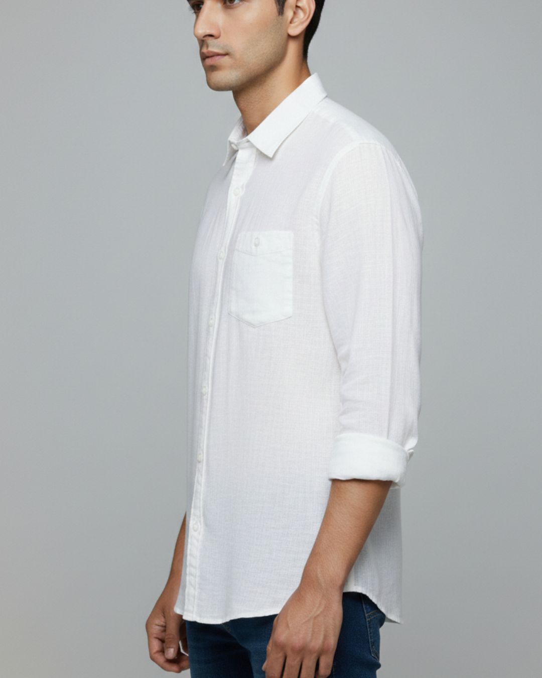 A man wearing a white long-sleeve button-down shirt with a chest pocket, shown in a side profile against a solid gray background.