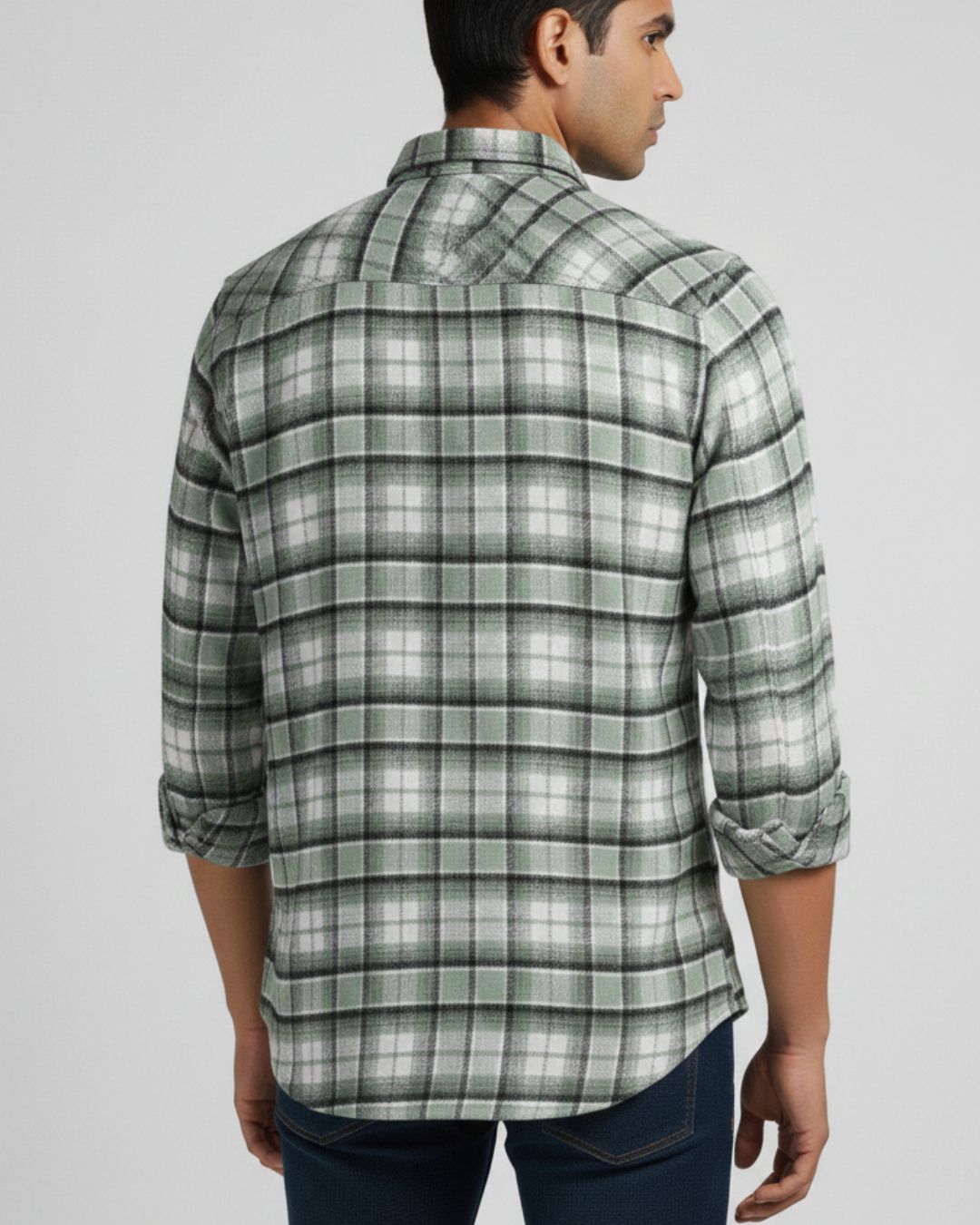 A man wearing a green and white plaid long-sleeve button-down shirt, shown from the back against a light gray studio background.