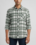 A man wearing a green and white plaid long-sleeve button-down shirt with dark blue jeans, shown from the waist up against a light gray background.