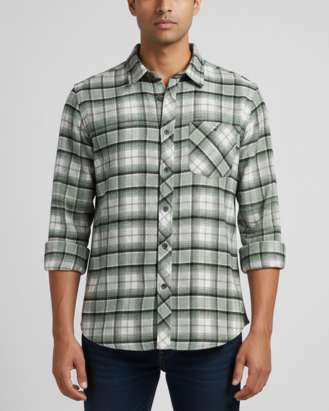 A man wearing a green and white plaid long-sleeve button-down shirt with dark blue jeans, shown from the waist up against a light gray background.