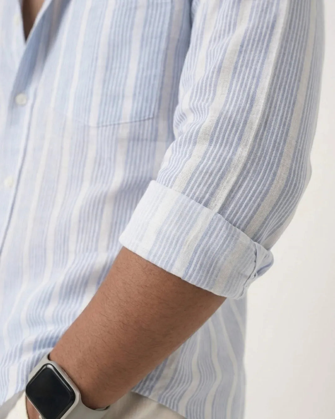 Close-up of a person wearing a light blue and white vertically striped long-sleeve button-up shirt with the cuff rolled up, showing the fabric texture and pattern.