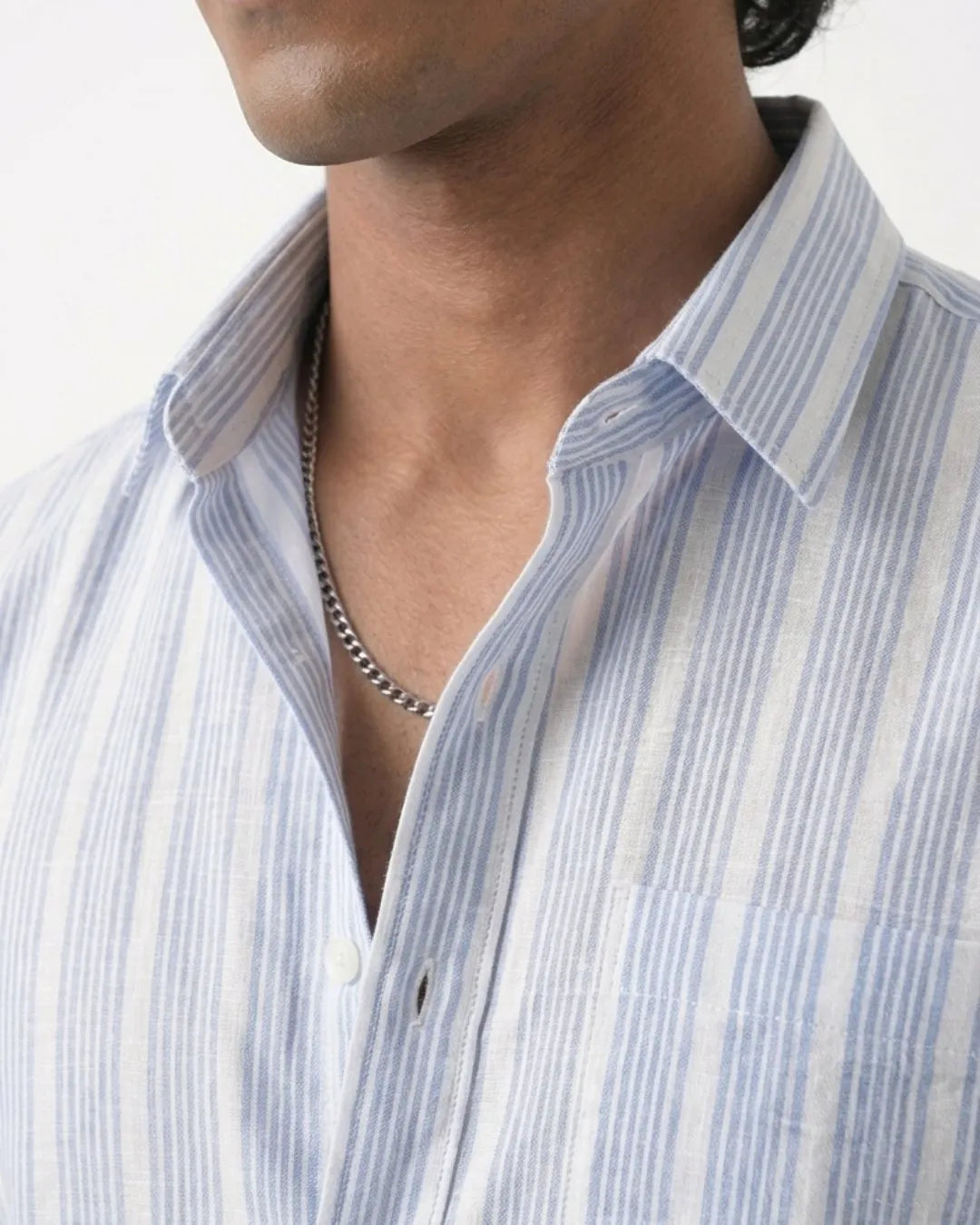 Close-up of a man wearing a light blue and white vertically striped button-down shirt with a silver chain necklace.