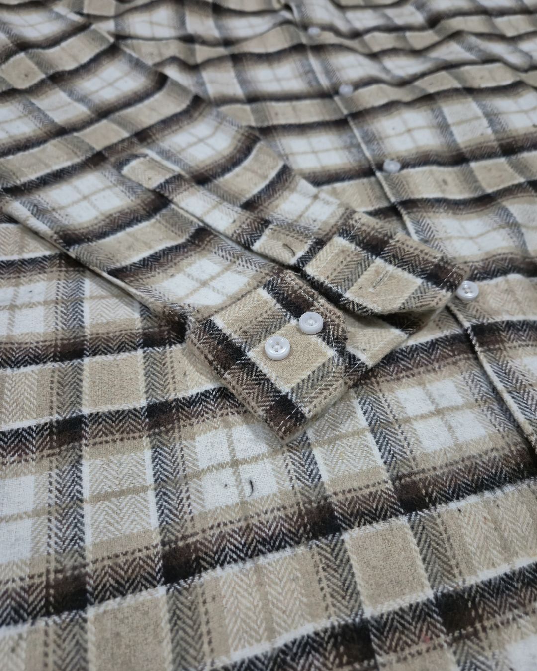 Close-up of a plaid button-up shirt in beige, brown, and white tones, showing the fabric texture and collar area.