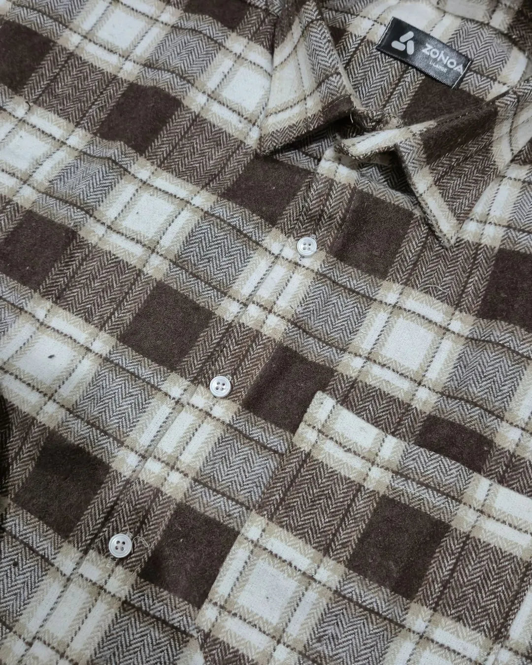 A close-up of a brown and beige plaid button-down shirt by ZONOA, showing the fabric texture, buttons, and collar.