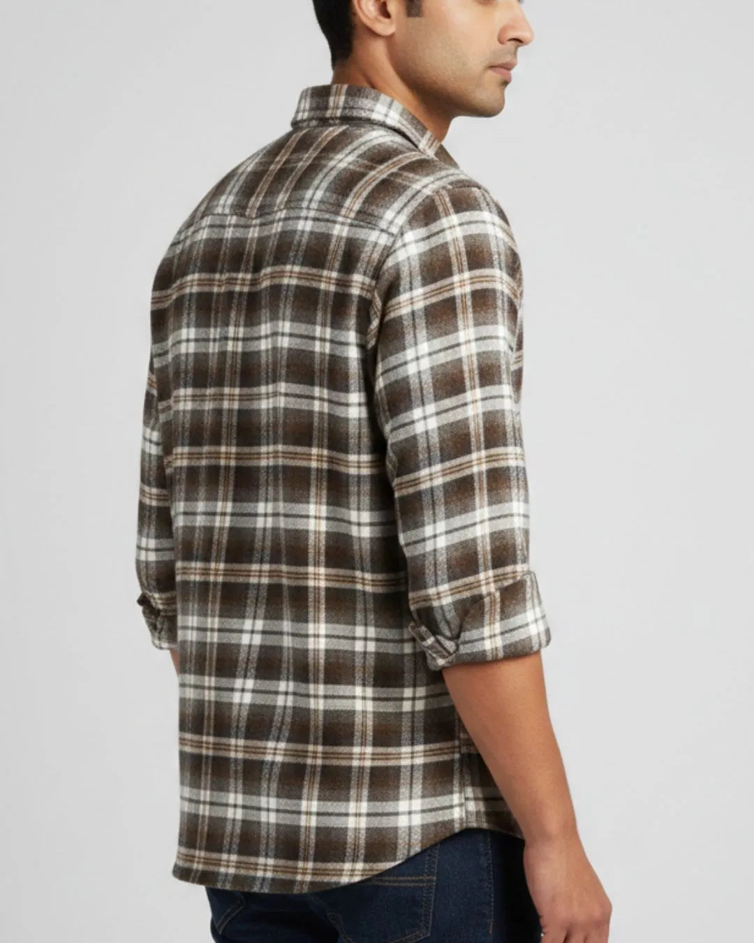 A man wearing a brown, beige, and white plaid button-down shirt, shown from a side-back angle against a light gray studio background.