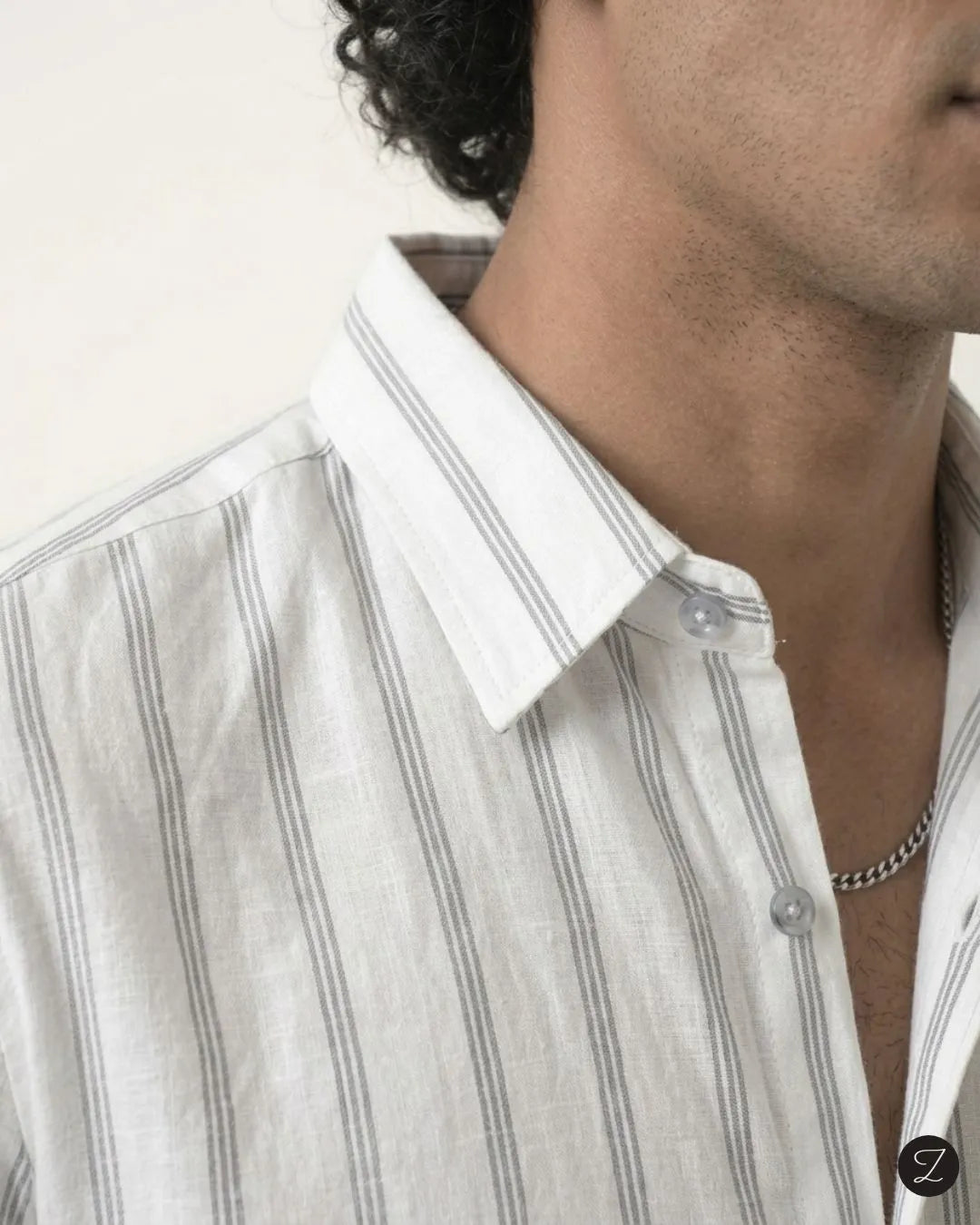 Close-up of a man wearing a white linen button-down shirt with thin vertical gray stripes, showing the collar, fabric texture, and part of his neck and chest.